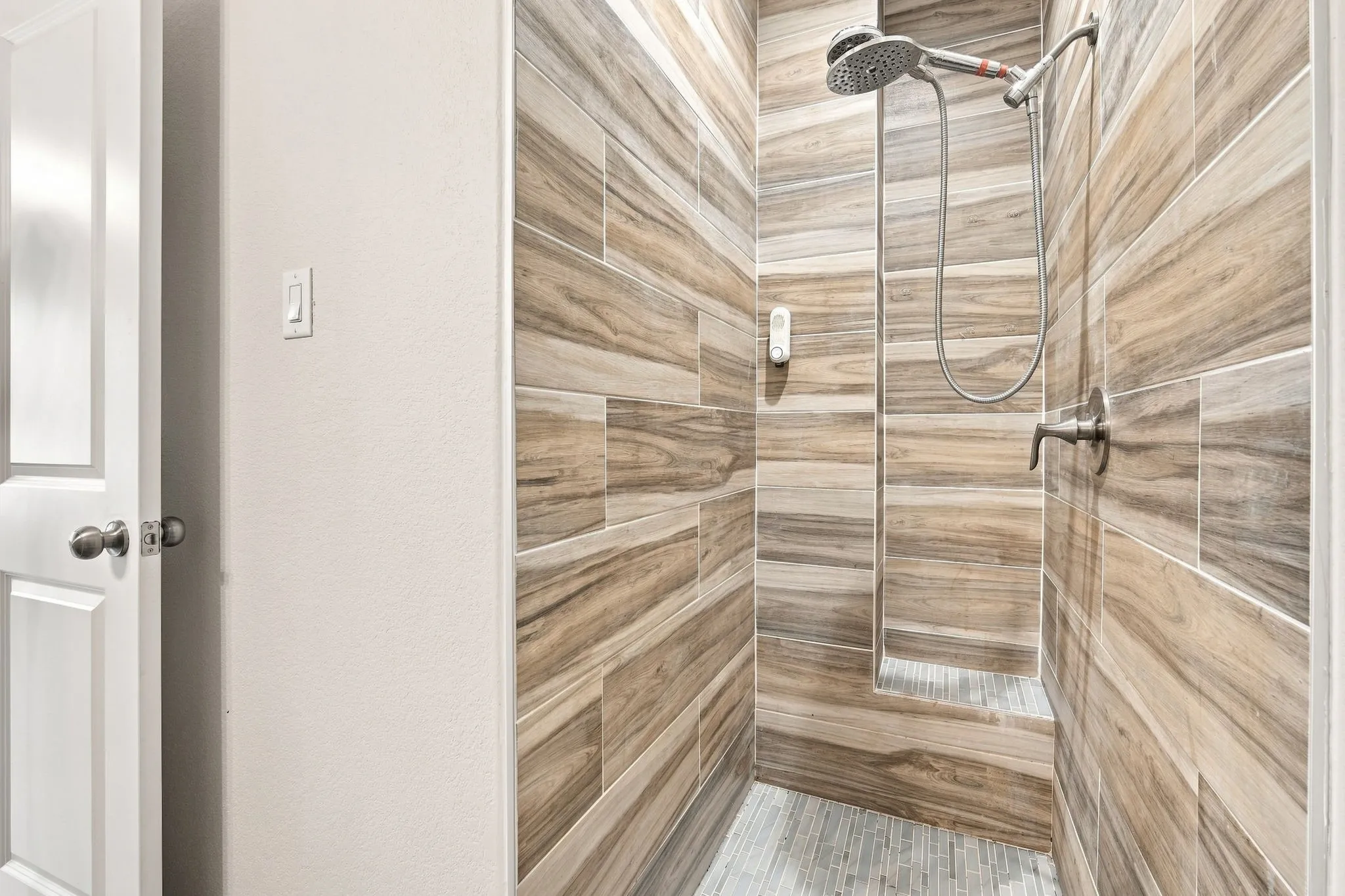 Walk-in shower with wood-finish tile surround, integrated shower bench, and a rain showerhead with handheld sprayer