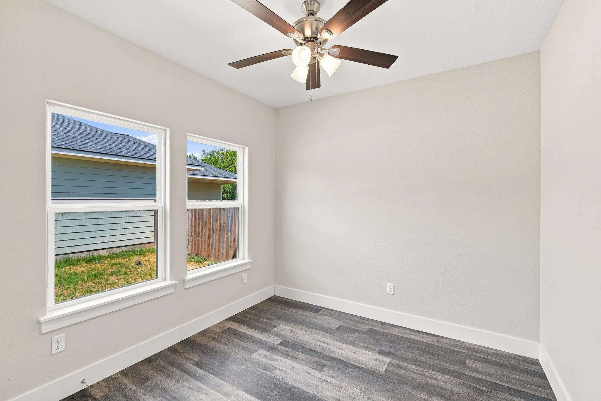 Wood-finish flooring, two large windows, white trim, and a ceiling fan with light fixture