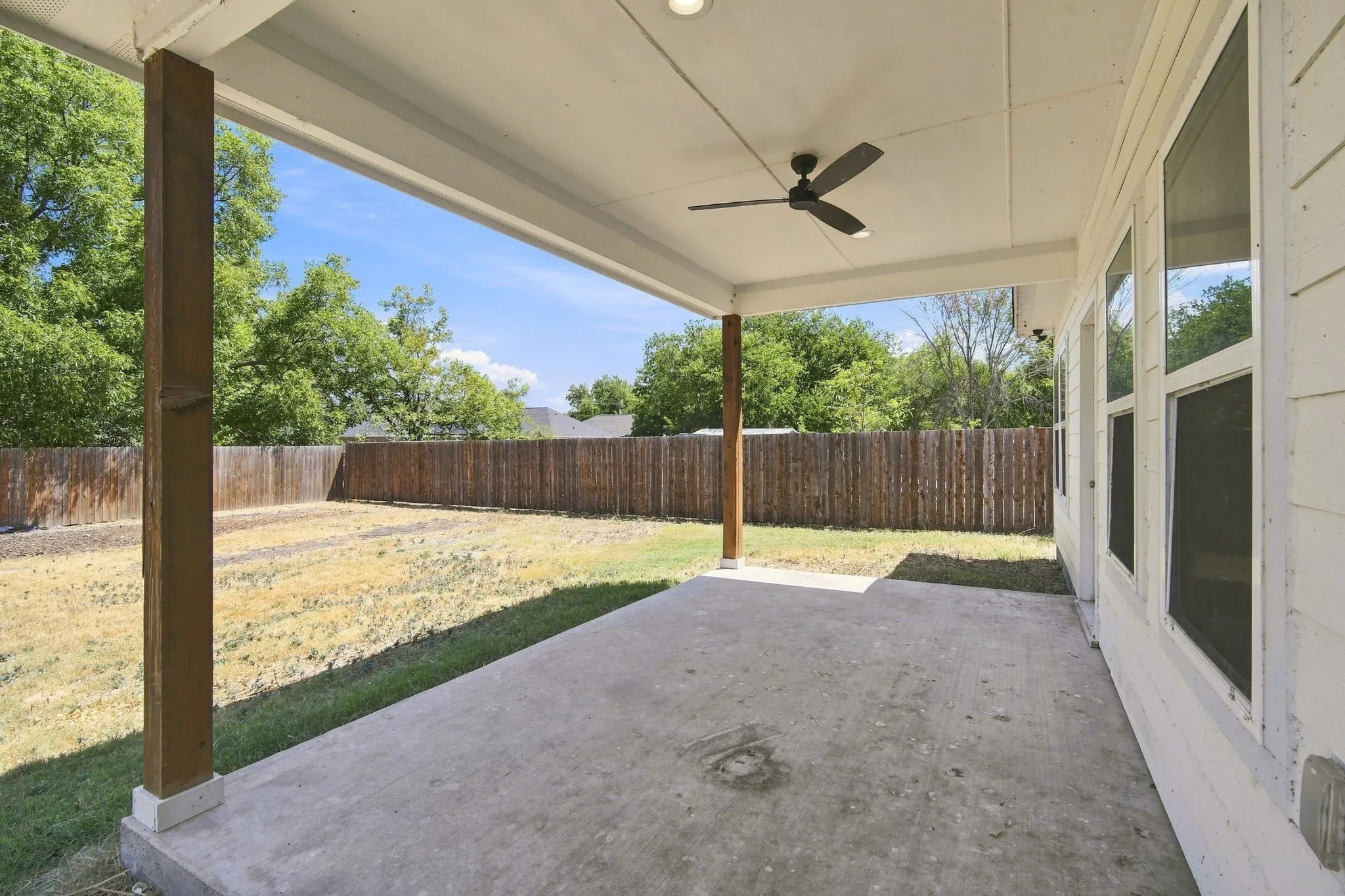 Covered patio with concrete flooring, wood posts, and a ceiling fan