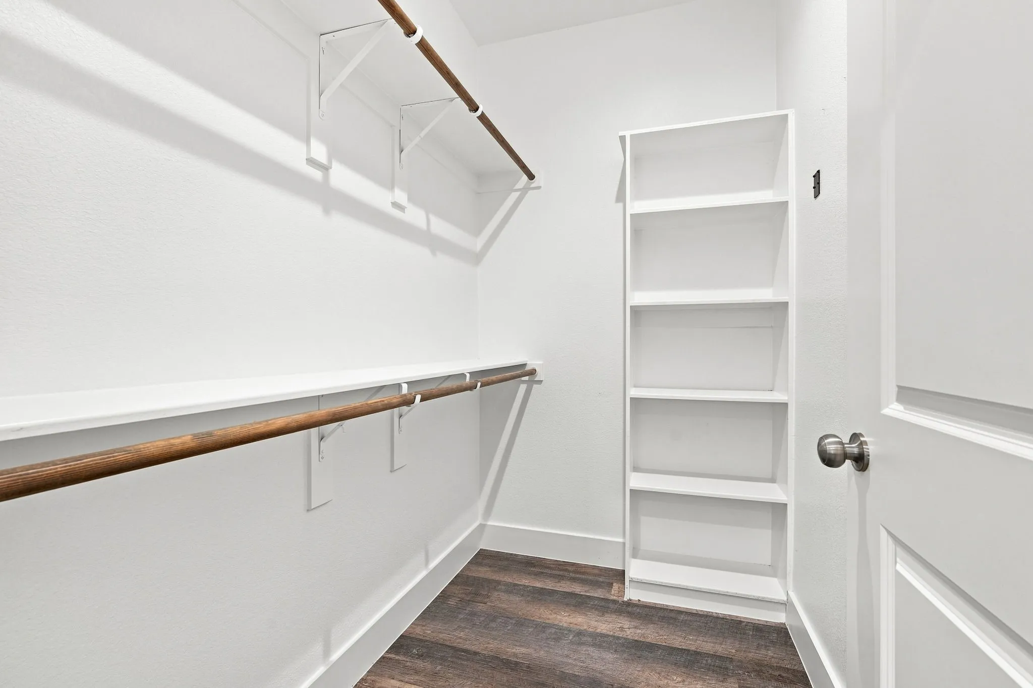 Walk-in closet with wood-finish flooring, built-in shelving unit, and multiple hanging rods