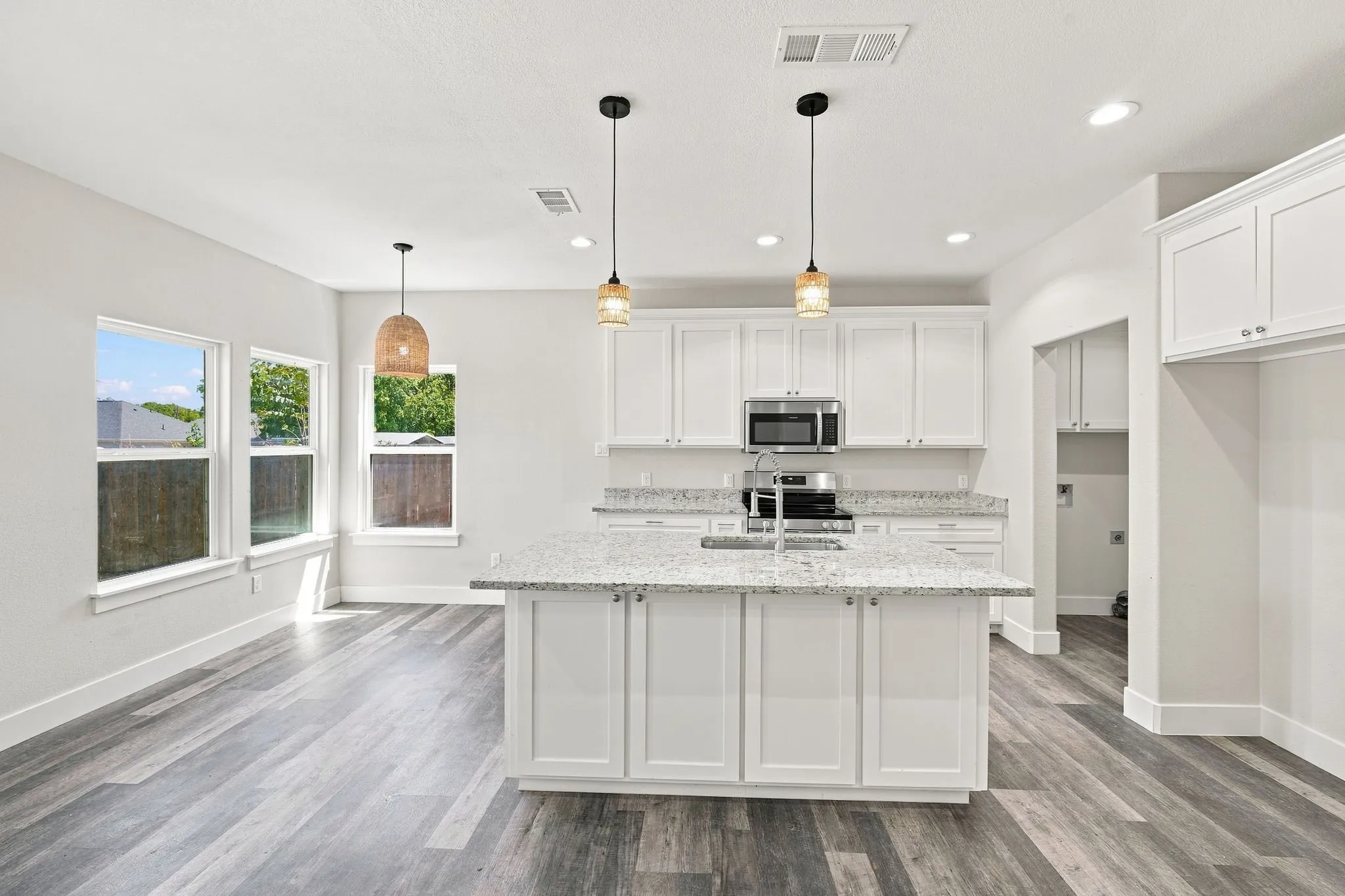 Kitchen featuring an island with built-in sink, white cabinetry, integrated stainless steel microwave, and wood-finish flooring