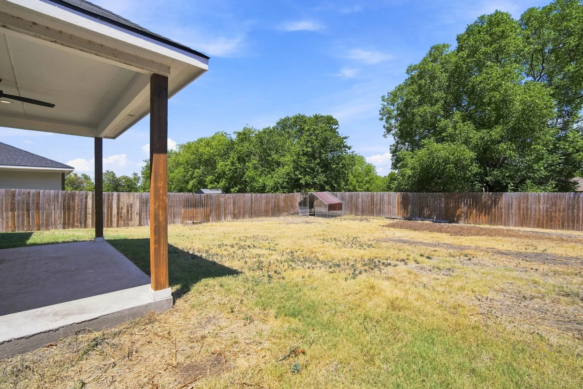 Expansive backyard featuring a wood privacy fence, concrete patio, and covered patio with a ceiling fan