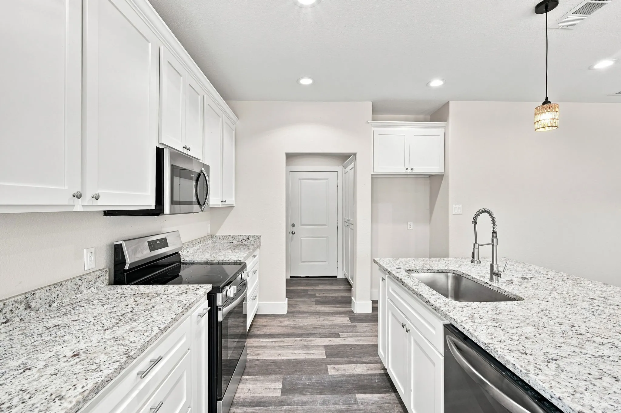 Kitchen featuring white shaker-style cabinetry, light granite countertops, stainless steel appliances, a kitchen island with an undermount sink, and wood-finish flooring
