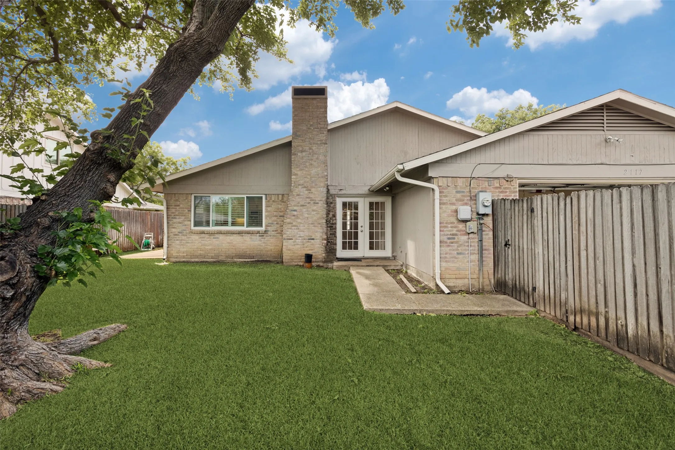 Large fenced backyard with shade tree and sprinkler system.