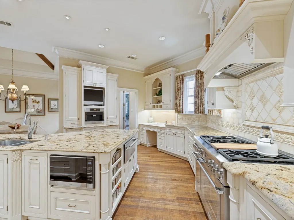 Spacious kitchen featuring an expansive center island, granite countertops, stainless steel appliances, custom cabinetry, and wood-finish flooring