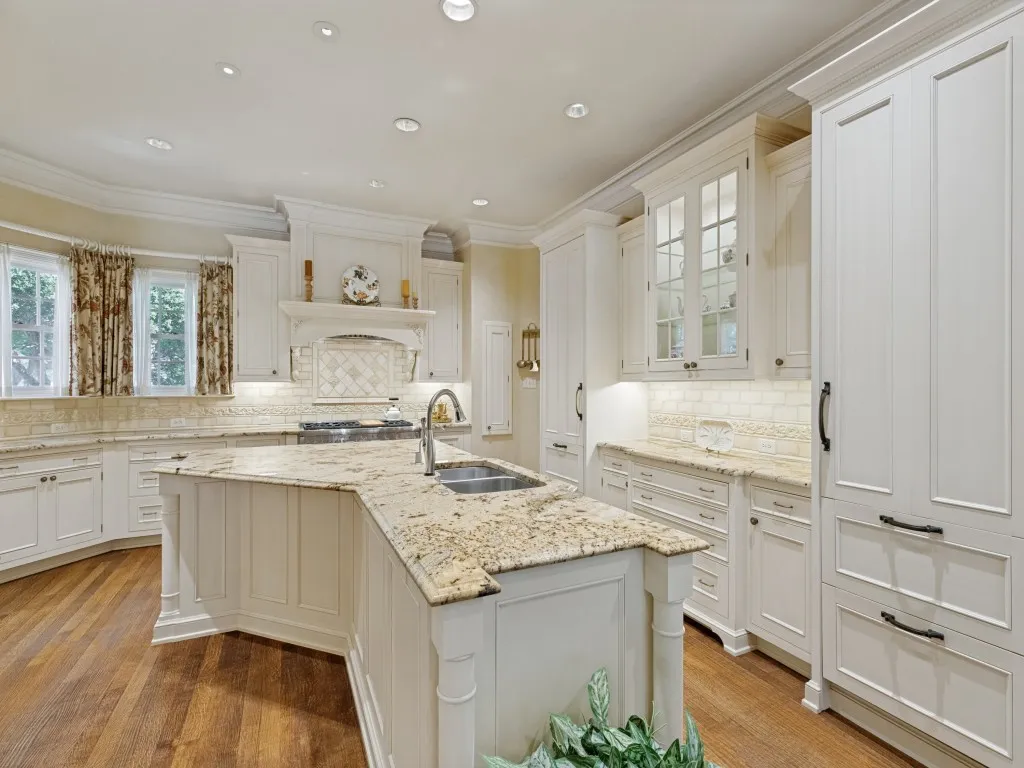Spacious kitchen featuring an expansive center island with an integrated sink, white cabinetry with panel detailing, light-toned stone countertops, and wood-finish flooring