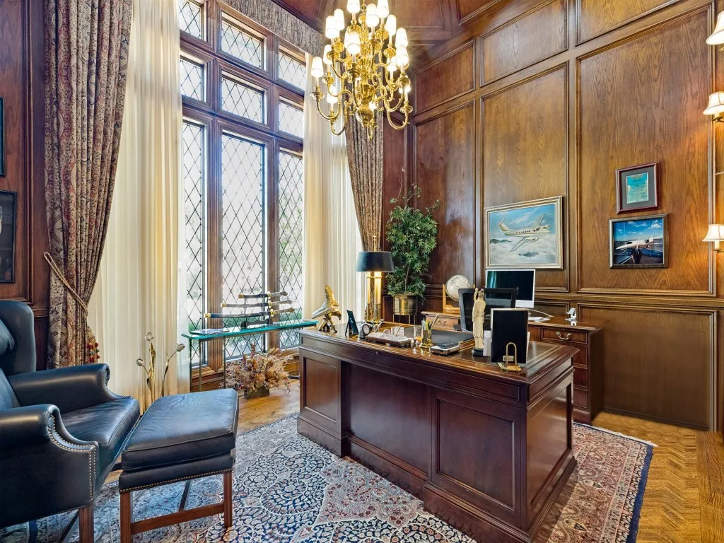 Wood paneling with decorative trim, large multi-pane windows with diamond-pattern detailing, chandelier lighting fixture, wood-finish flooring, and built-in wall sconces