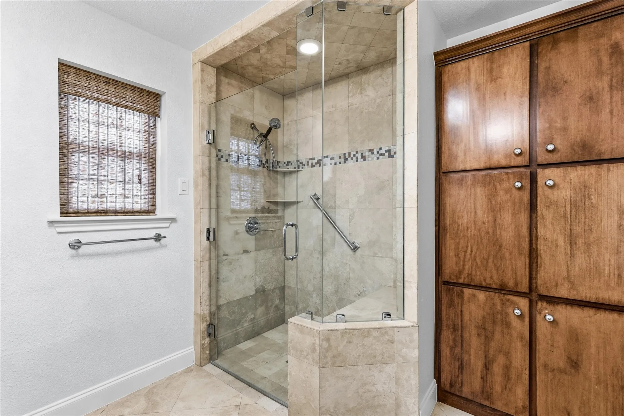 Curbless walk-in glass front shower with seat also featuring the custom linen tower...