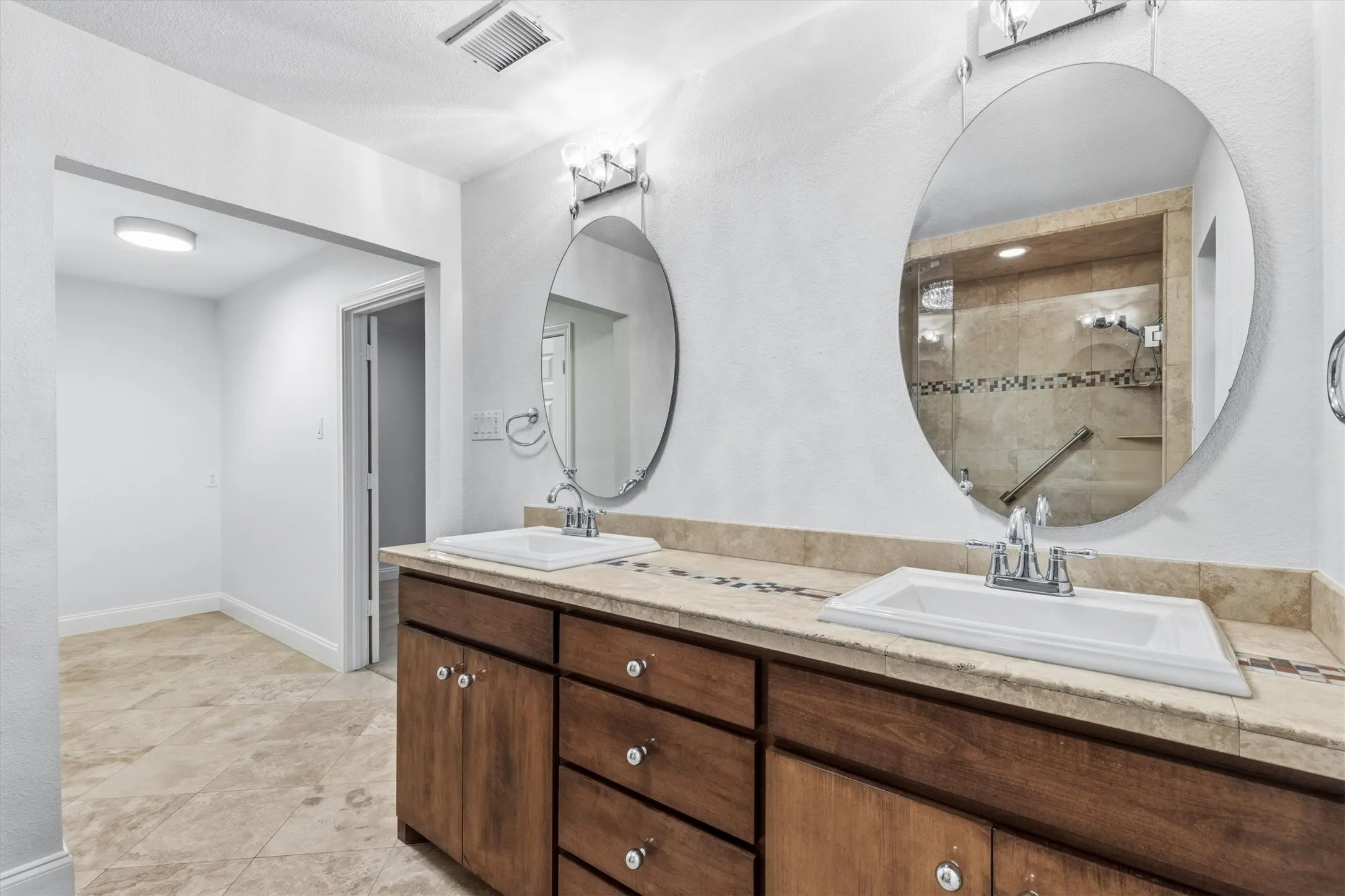Primary bath with custom cabinets, dual sinks, travertine stone and dressing area featured....*virtually staged to show potential*