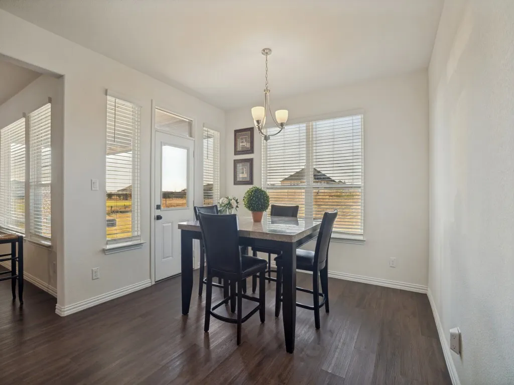 Dark wood-finish flooring with white baseboards, a light fixture with three sconces, and multiple windows with horizontal blinds