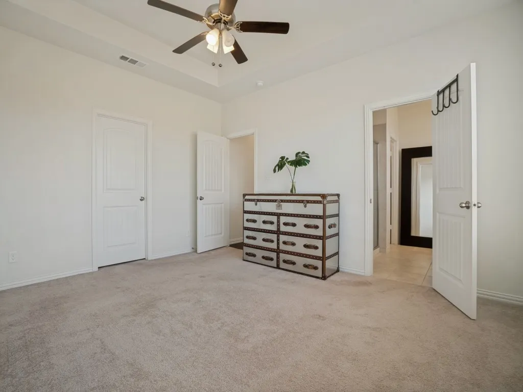 Spacious primary bedroom featuring neutral carpeting, ceiling fan with integrated lighting, and multiple closet entries with six-panel white doors
