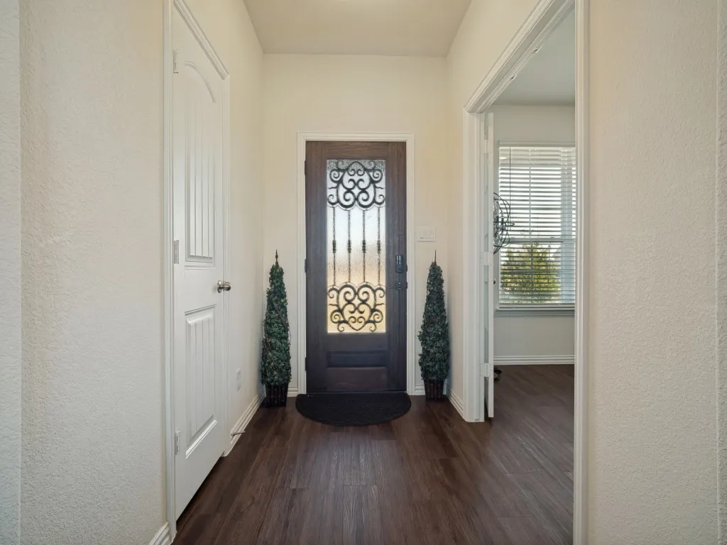 Dark wood-finish flooring, white painted walls, and a decorative front door with an ornate wrought iron insert