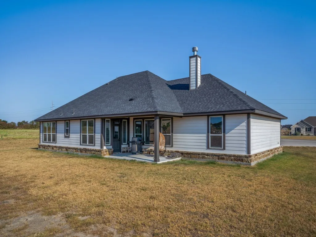 Light-colored siding exterior with a dark shingle roof, stone foundation, and a covered back patio