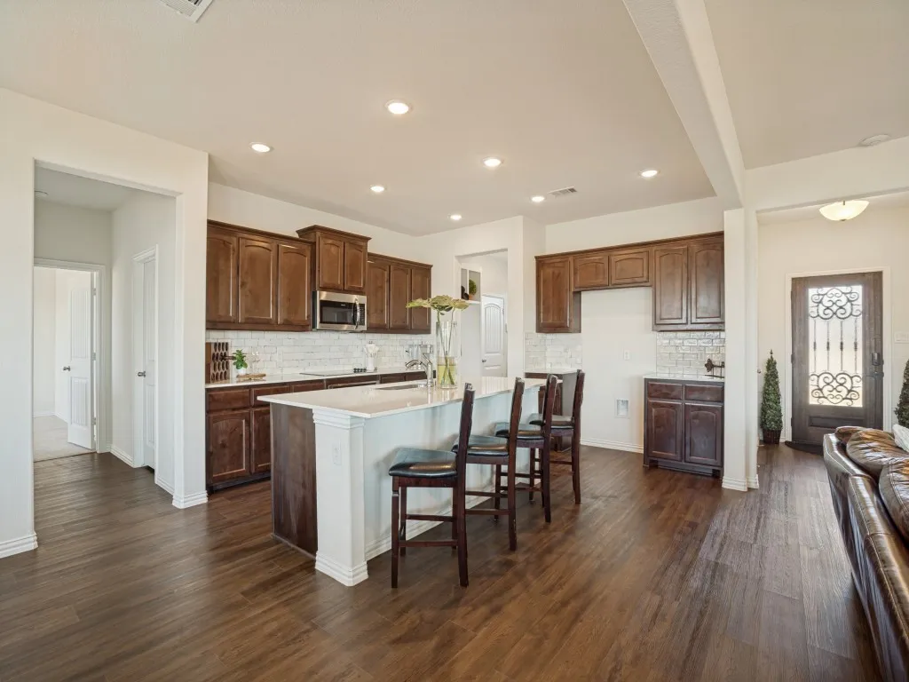 Kitchen featuring wood-finish flooring, dark wood cabinetry, a white tile backsplash, an island with seating, and recessed lighting