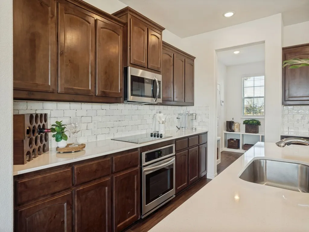 Kitchen featuring wood-finish cabinetry, stainless steel appliances, white subway tile backsplash, and light-toned countertops