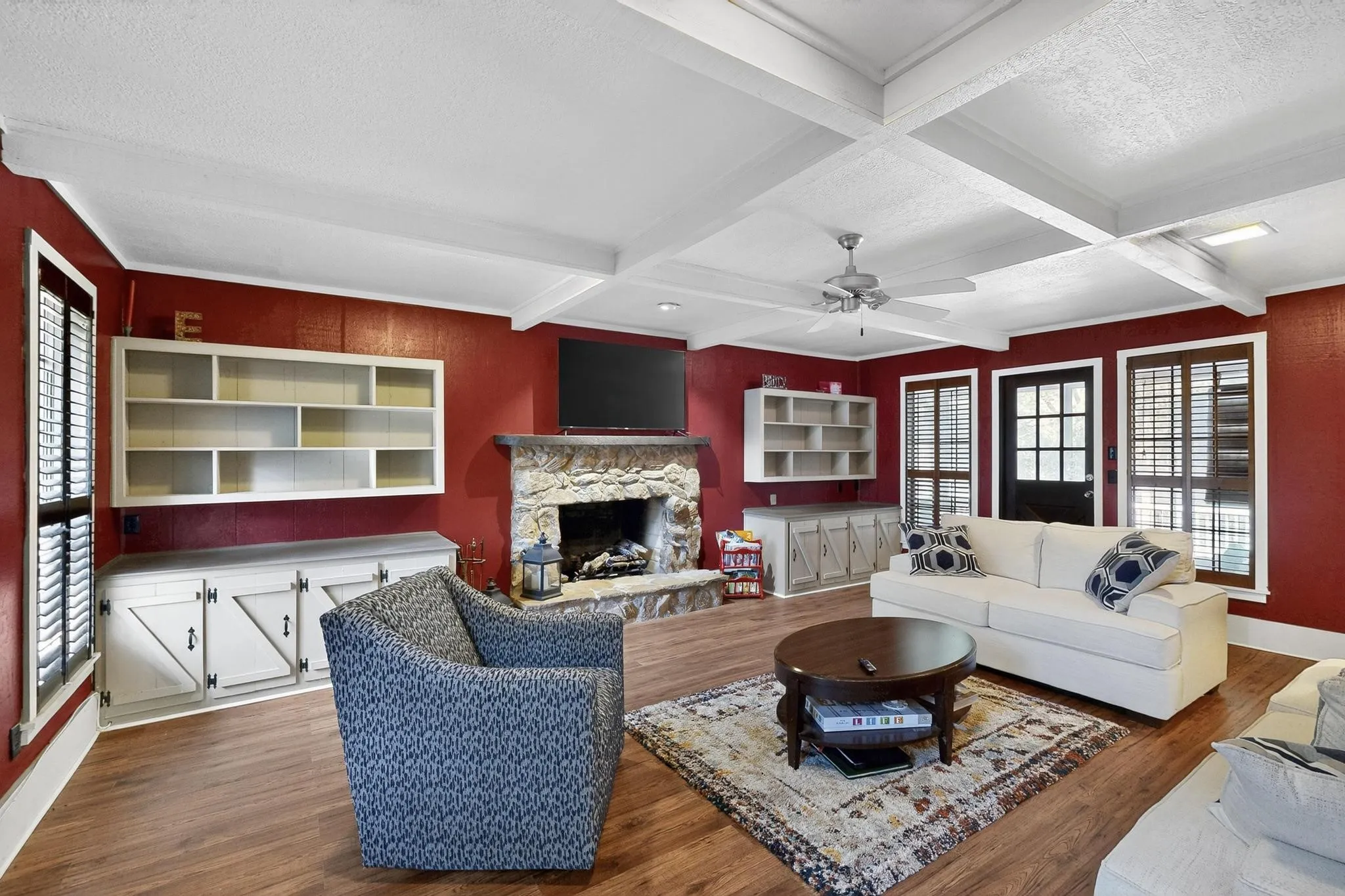 Living room featuring dark wood finished floors, beam ceiling, a stone fireplace, coffered ceiling, and a textured ceiling