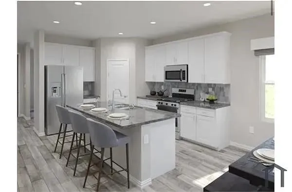 Kitchen featuring an expansive island with a sink, stainless steel appliances, abundant white cabinetry, a stone-finish backsplash, and wood-finish flooring