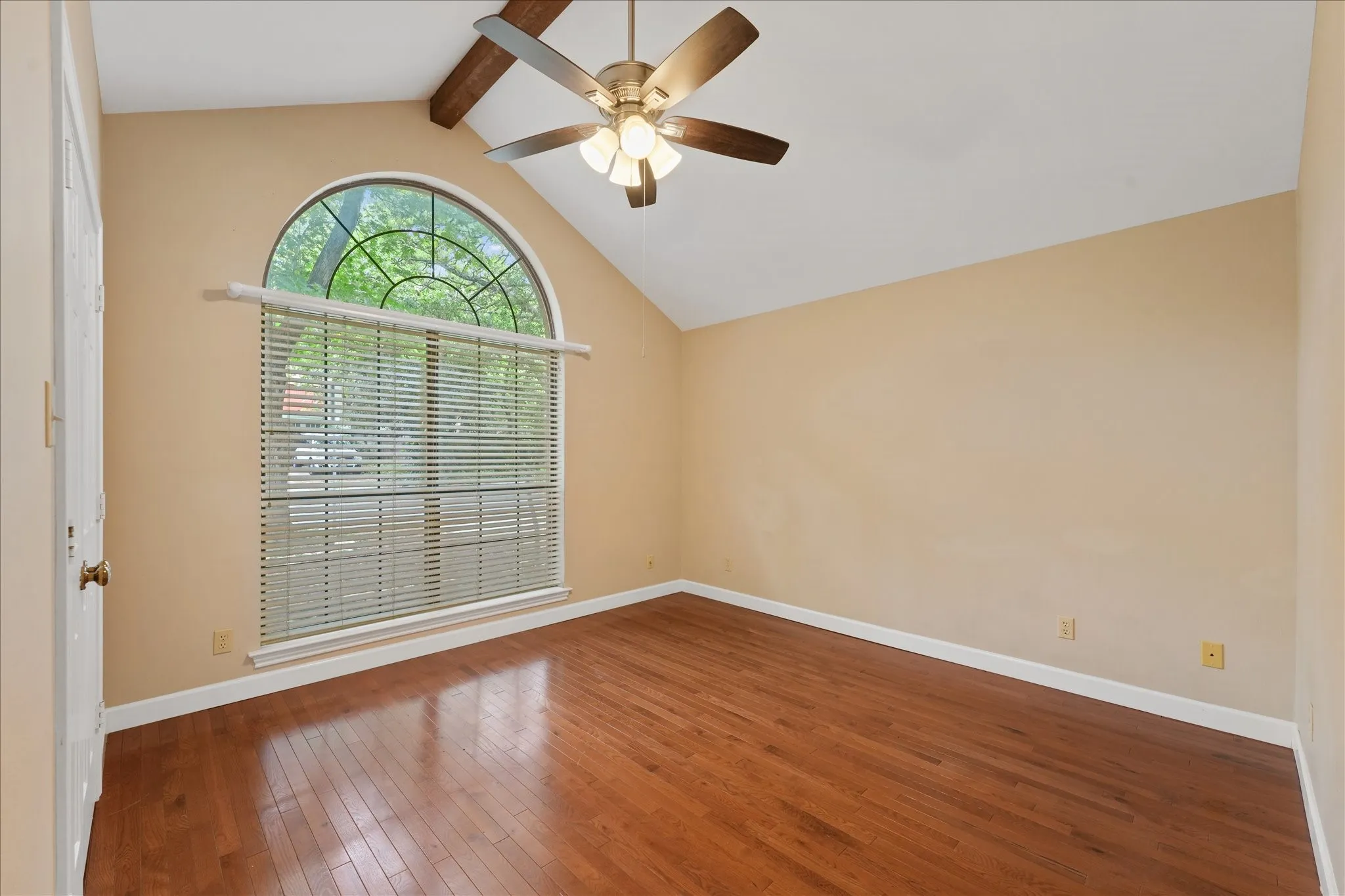 Front flex room with vaulted ceiling, exposed beam, hardwood floors, and oversized arched window ideal for home office, second living area, or third bedroom.