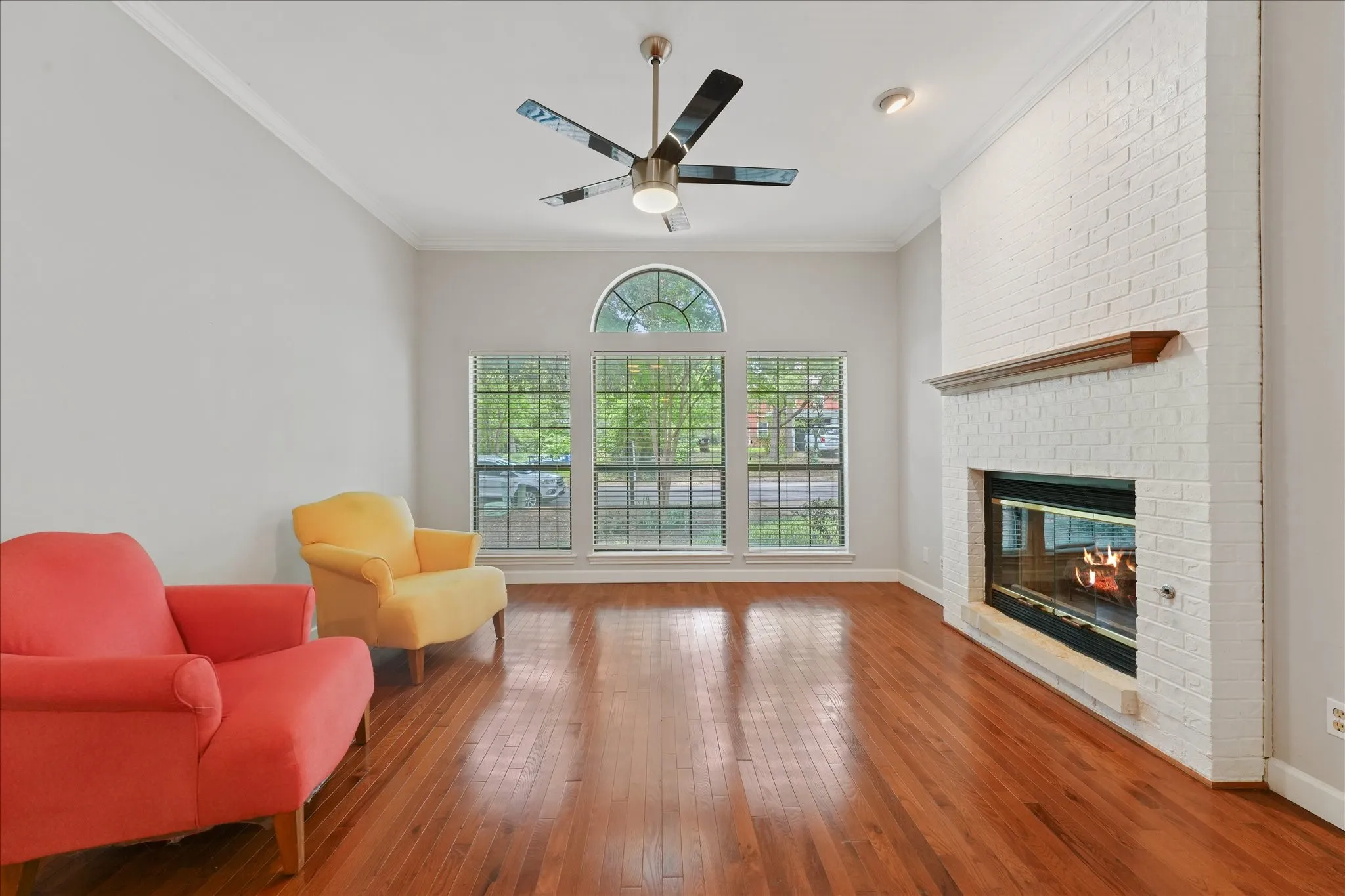 Spacious living room with hardwood floors, tall ceilings, gas fireplace, oversized windows, and abundant natural light overlooking the front yard.