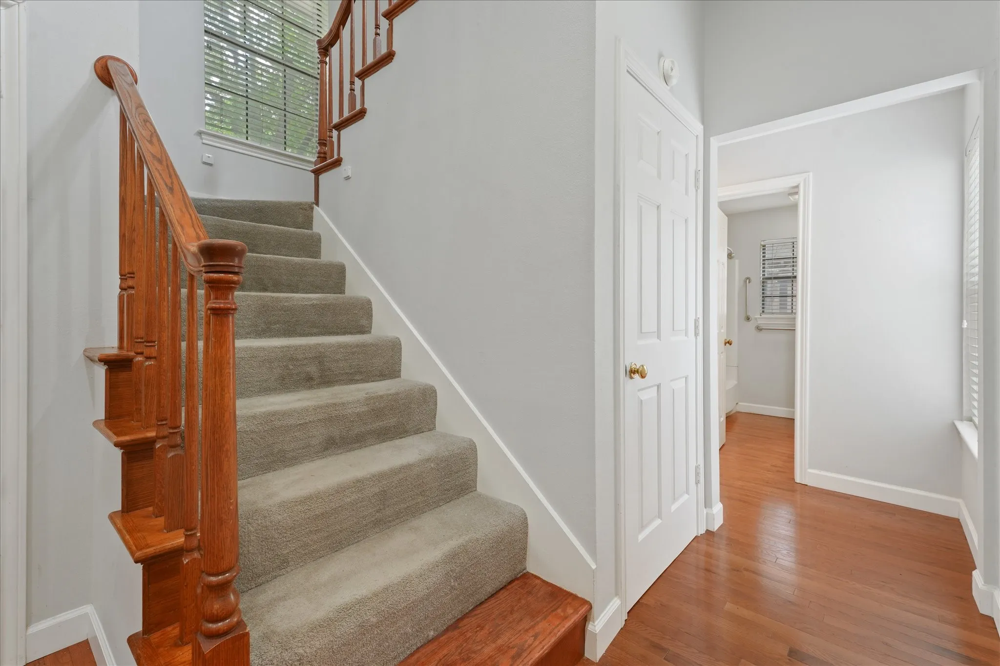 Staircase and hallway with hardwood flooring, neutral paint tones, and natural light connecting the downstairs living spaces.