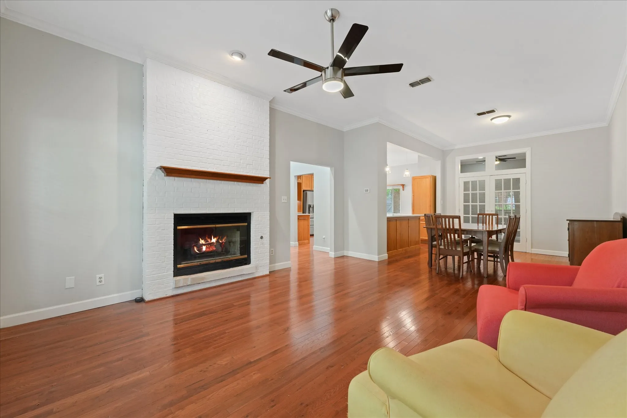 Open-concept living and dining area with hardwood flooring, painted brick fireplace, and flexible layout for entertaining or everyday living.
