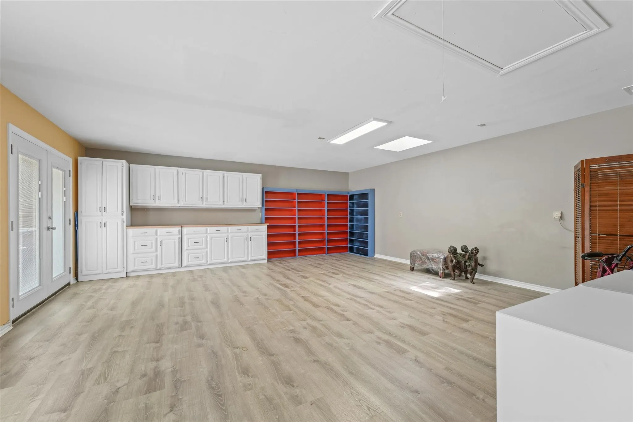 Large flex room with luxury vinyl plank flooring, extensive built-in storage, skylights, and French doors with private exterior access ideal for game room, studio, gym, office, or second living space.