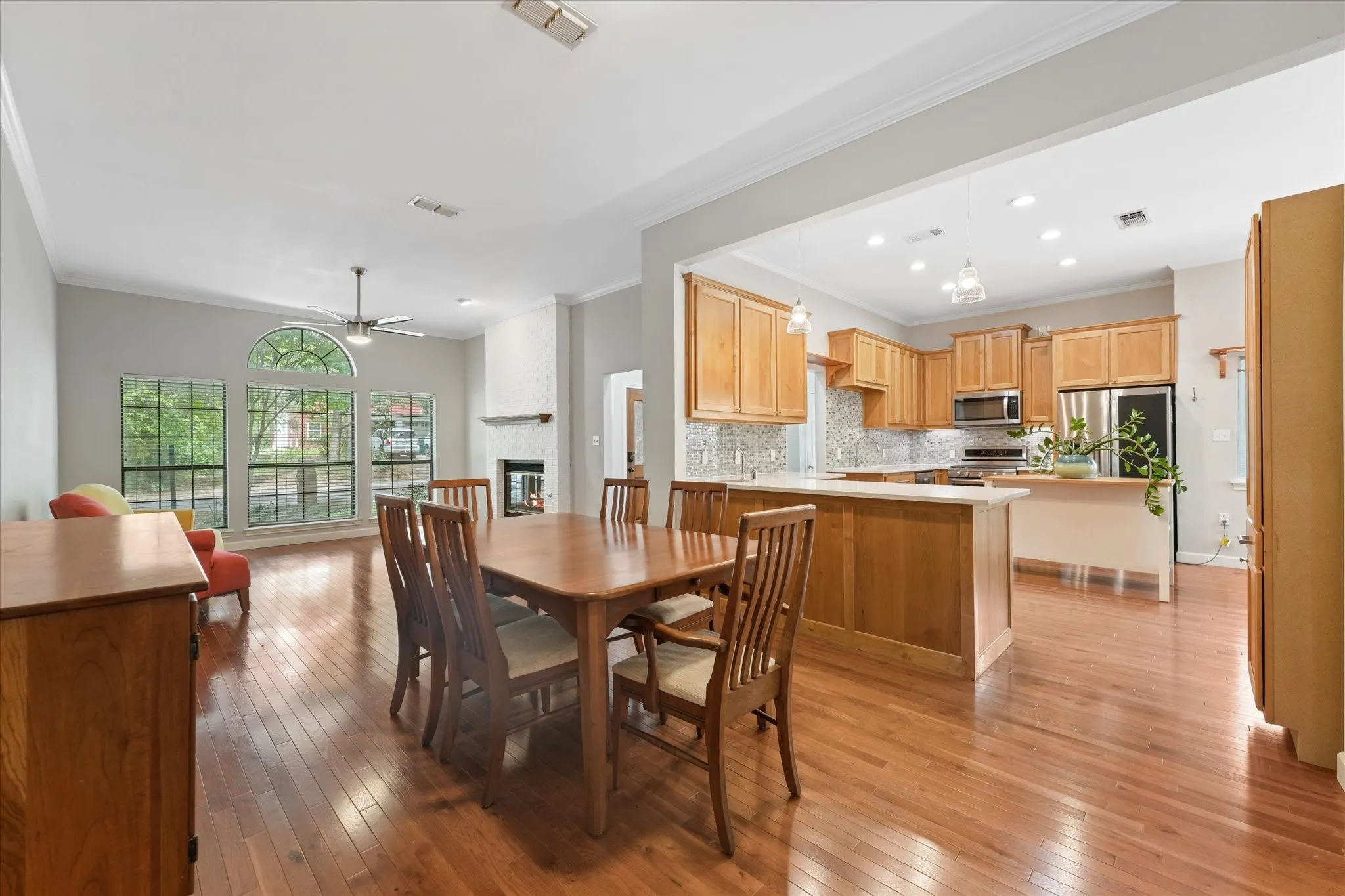 Spacious open living, dining, and kitchen layout with hardwood flooring, tall ceilings, gas fireplace, and abundant natural light throughout.