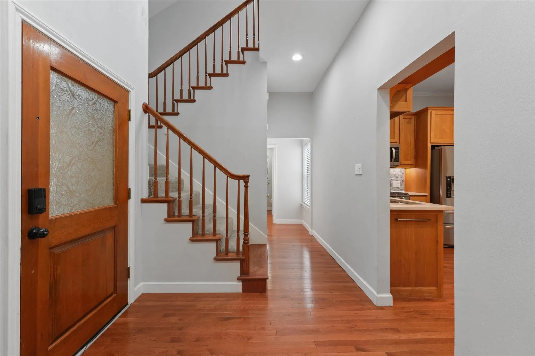 Bright entryway with hardwood floors, updated paint, wood staircase, and open flow into the main living and kitchen areas.