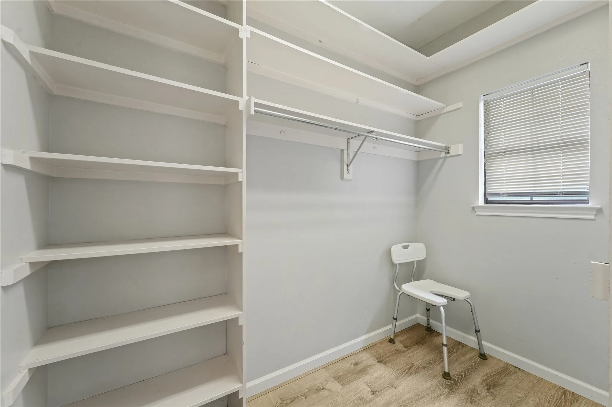 Large walk-in closet with custom built-in shelving, hanging space, and window for natural light and added functionality.
