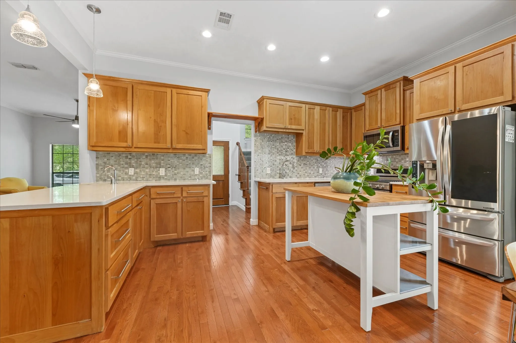 Updated kitchen featuring custom cabinetry, modern hardware, stainless steel refrigerator, tile backsplash, and multiple prep and serving areas.