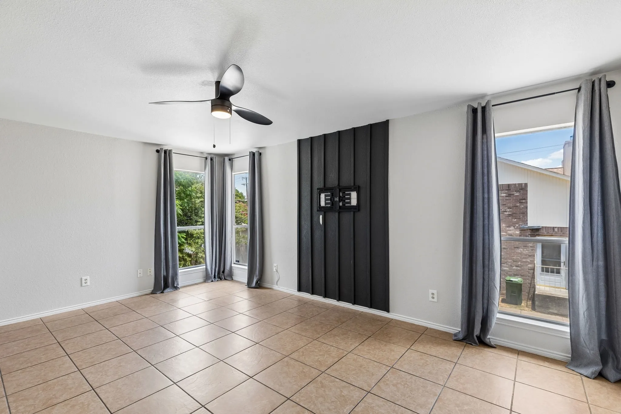 Spacious room featuring neutral tile flooring, a modern ceiling fan, and multiple windows