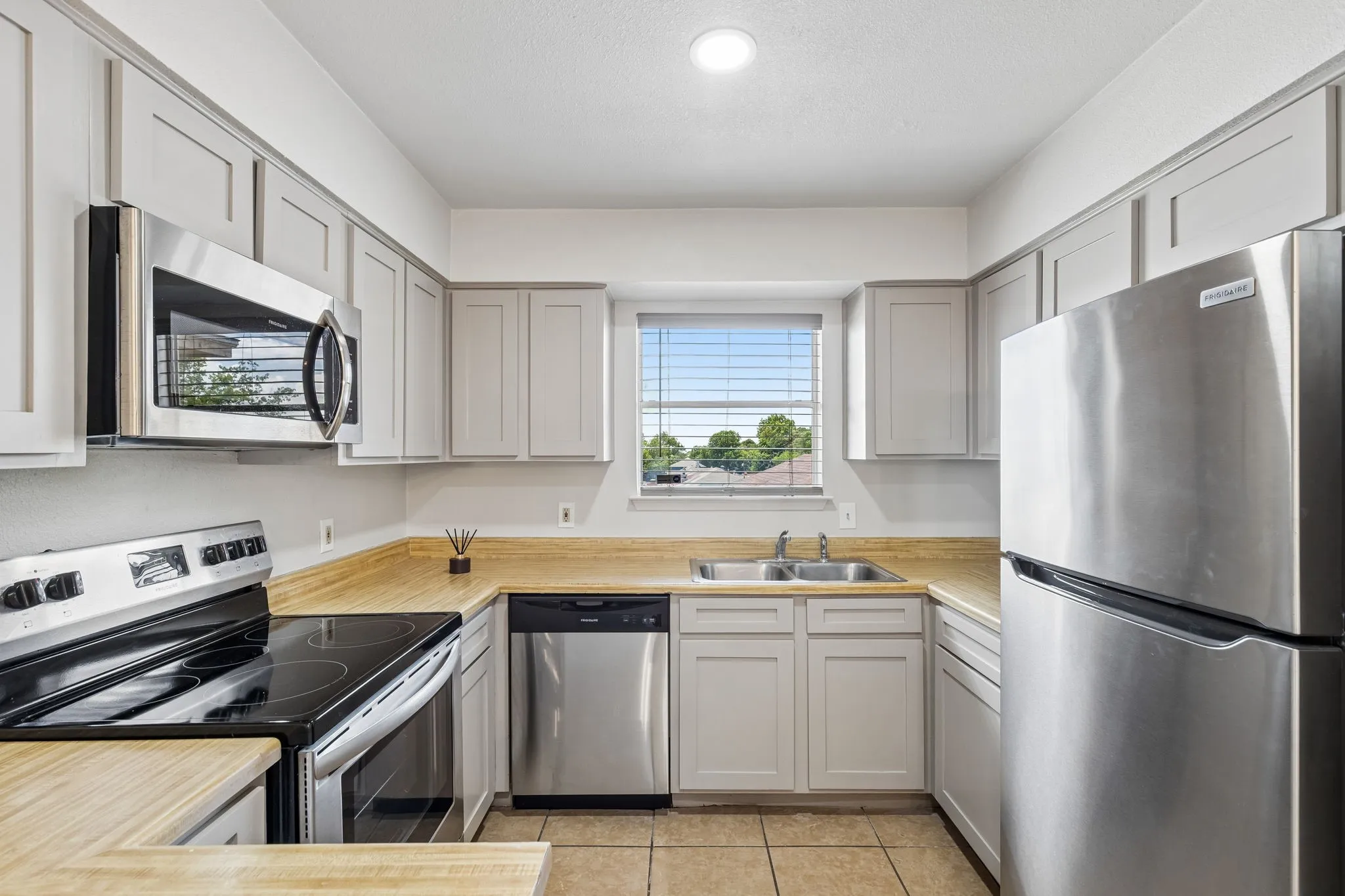 Kitchen featuring light-toned cabinetry, stainless steel appliances, wood-finish countertops, and tiled flooring
