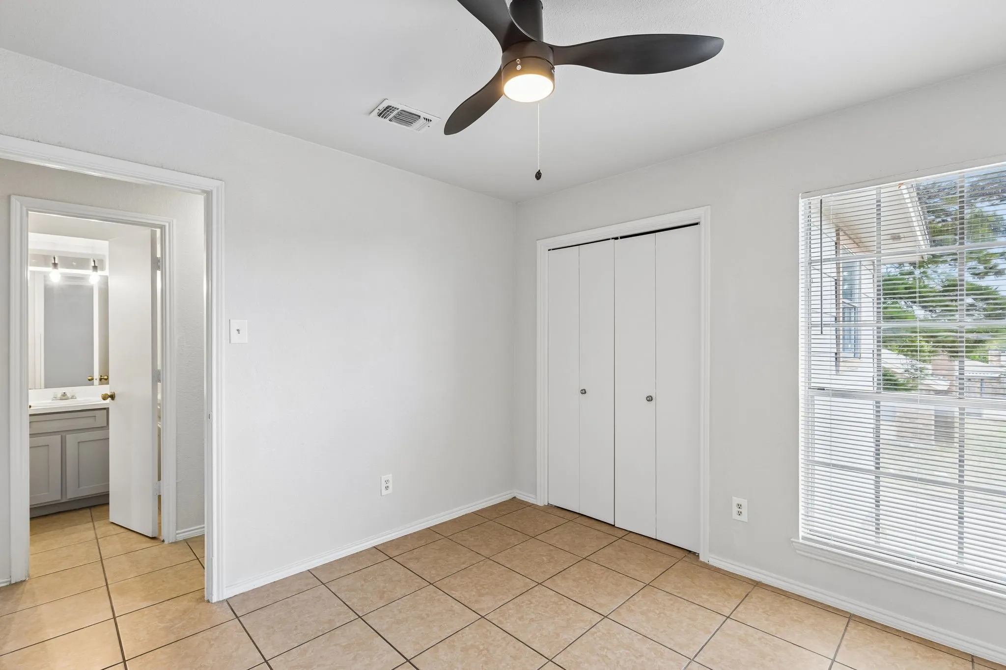 Tile flooring, ceiling fan, white bi-fold closet doors, and large window with blinds