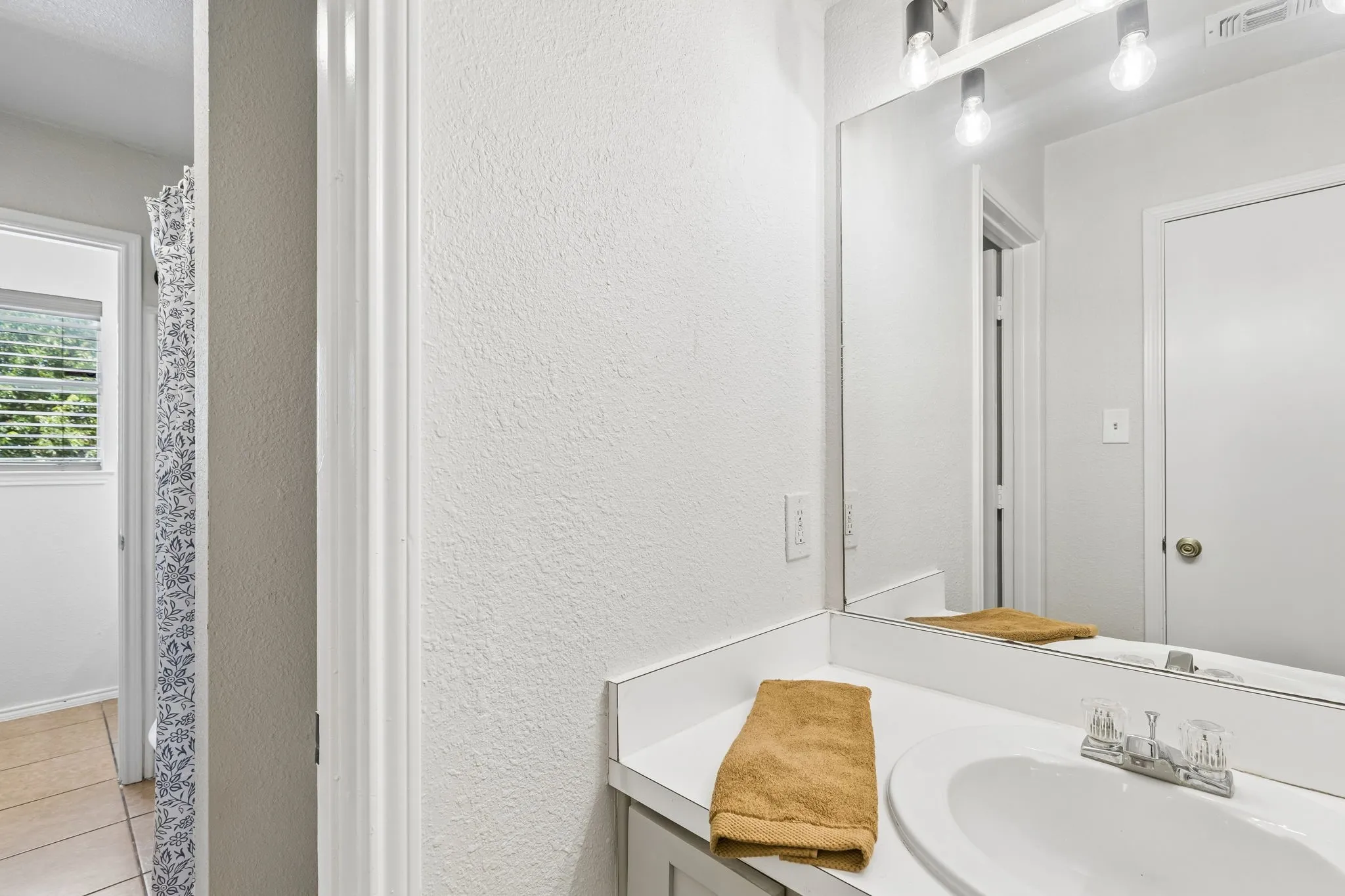 Vanity with integrated sink, chrome faucet, and expansive mirror with overhead lighting