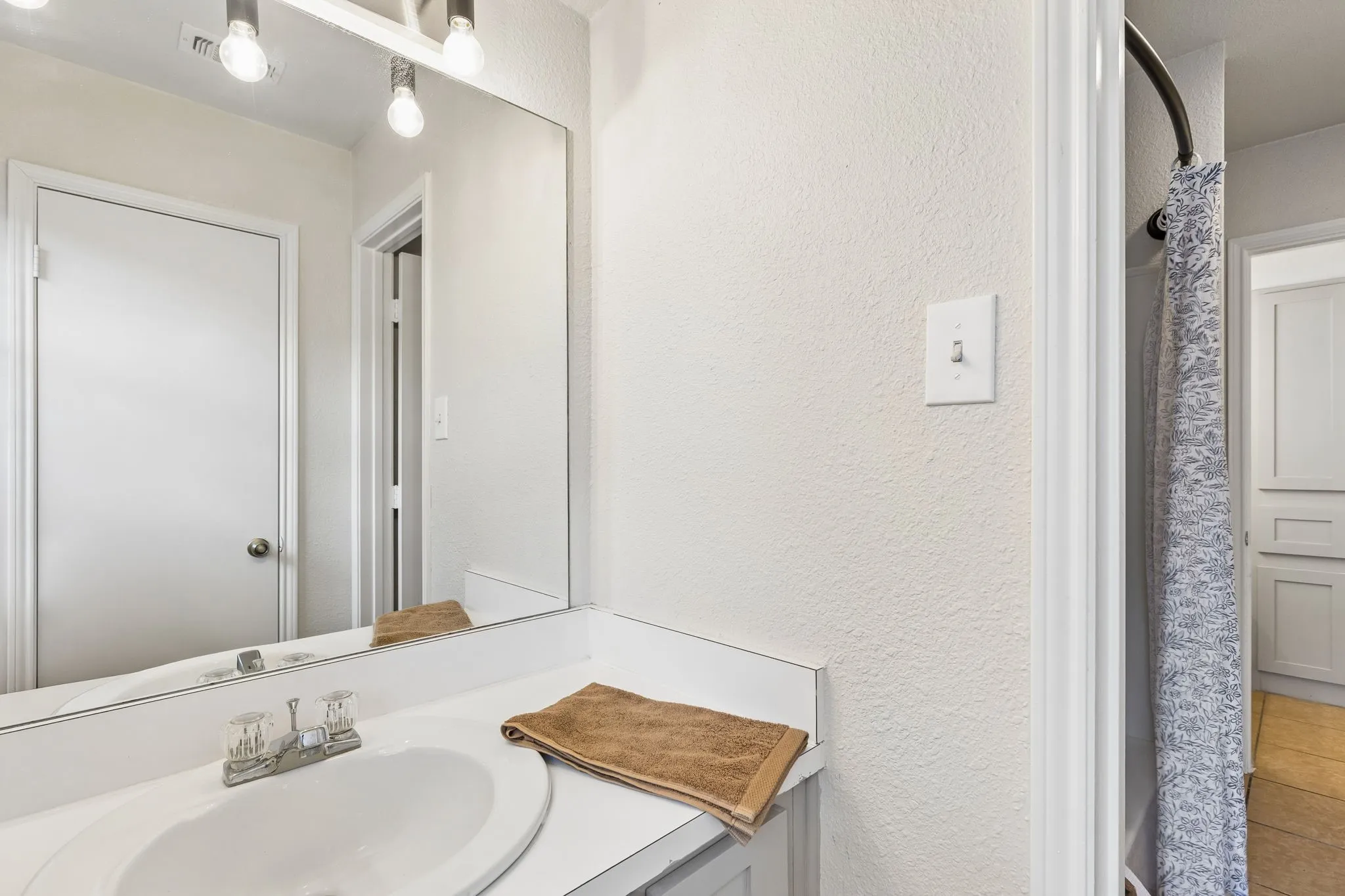 Vanity with integrated sink, chrome faucet, and expansive wall-mounted mirror
