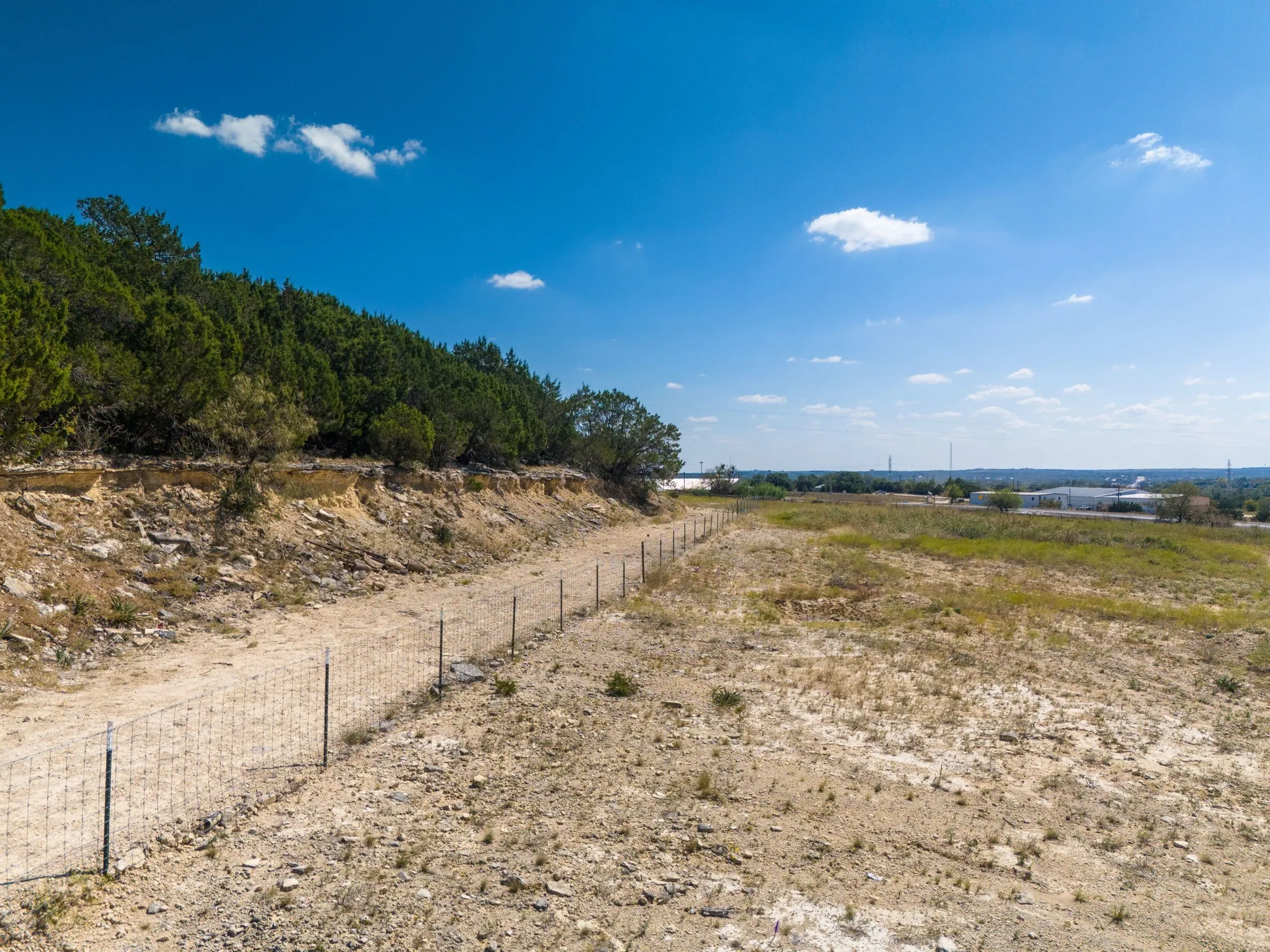Expansive undeveloped land with a wire fence, natural ground cover, and a treed hillside