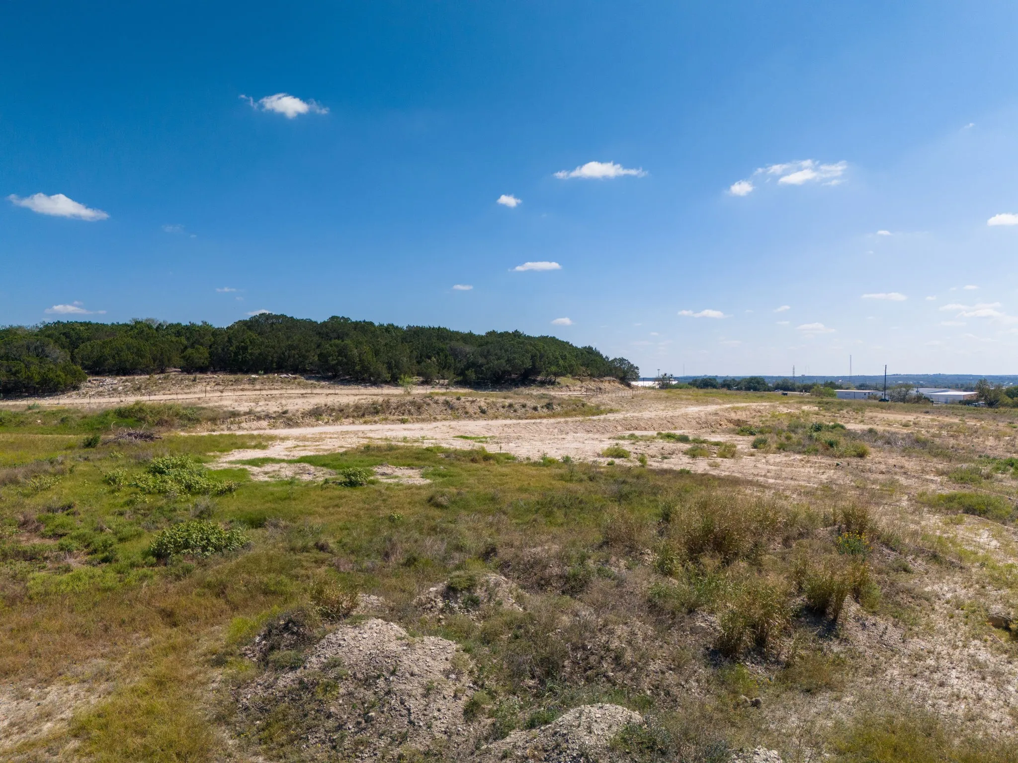 Expansive land parcel featuring natural ground cover, treed perimeter, and distant structures