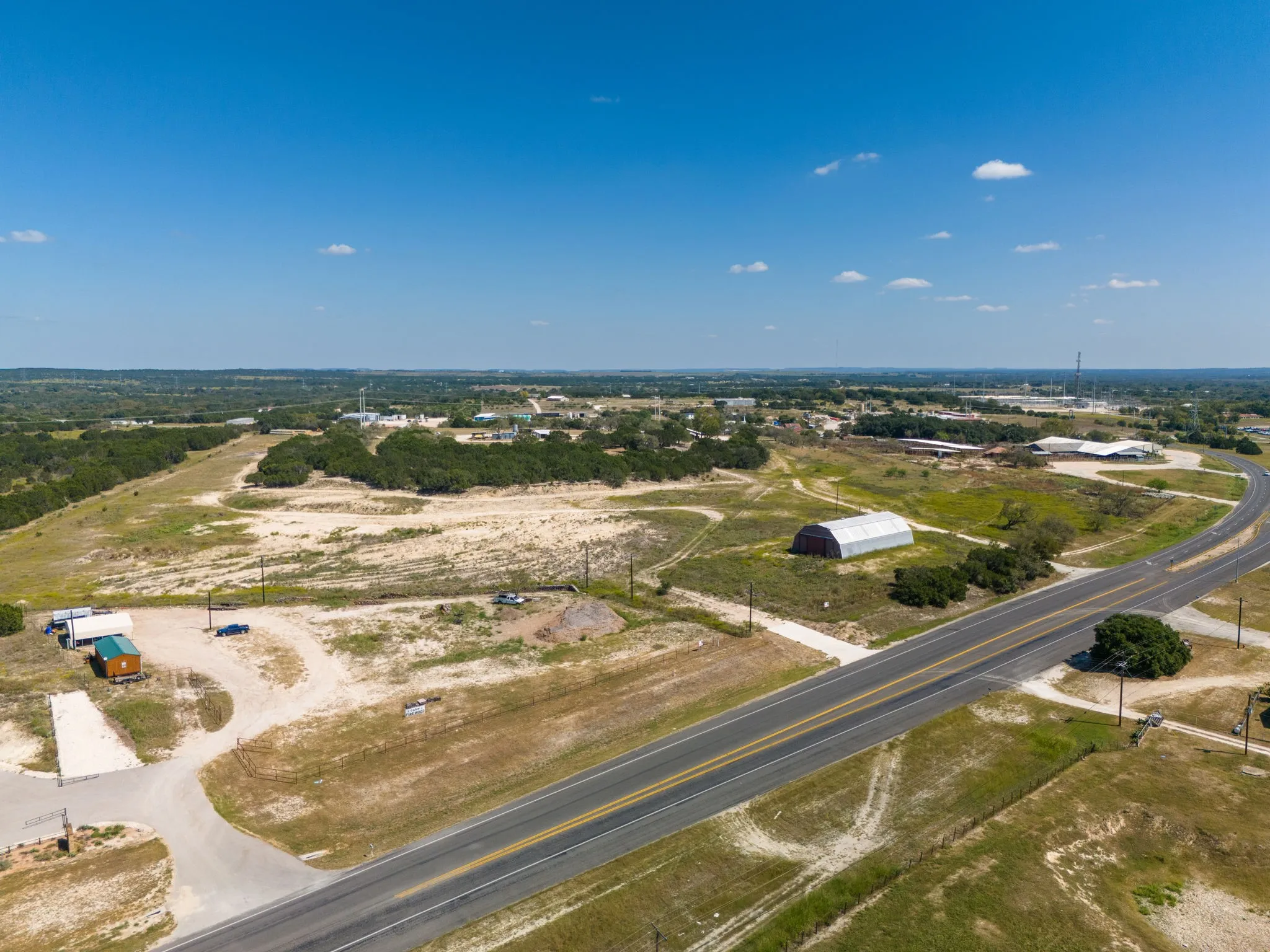 Expansive land parcel featuring paved road frontage, natural vegetation, and a clear blue sky