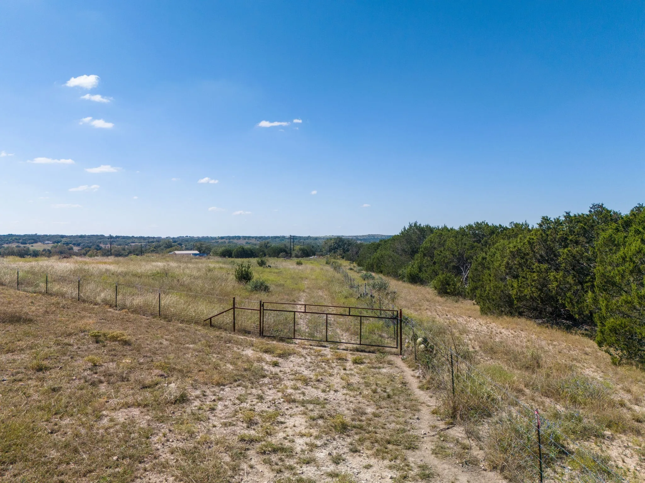 Expansive land parcel featuring a metal gate, perimeter fencing, and mature trees along the property line