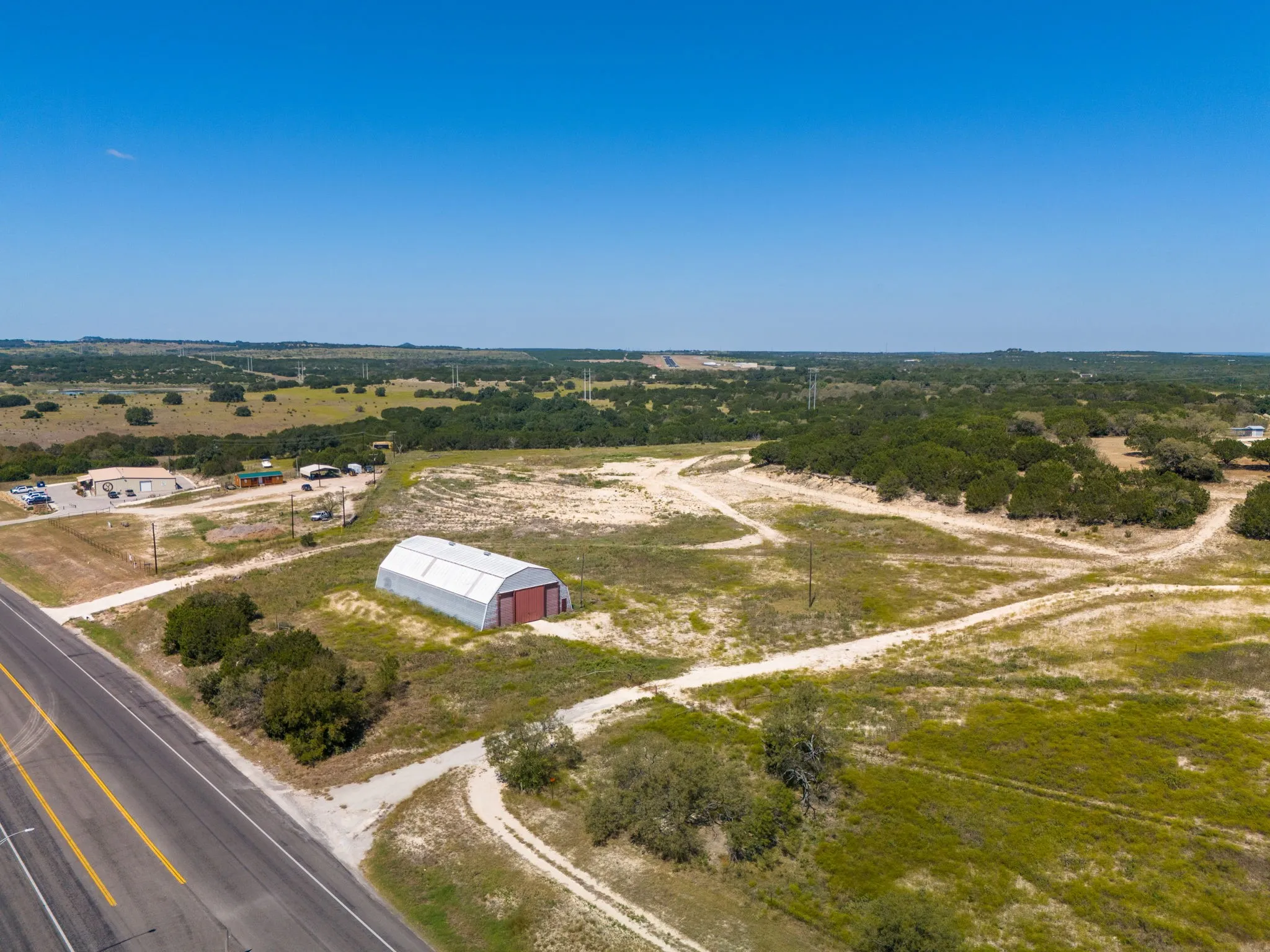 Expansive land parcel featuring a metal Quonset hut, mature trees, and a paved road frontage