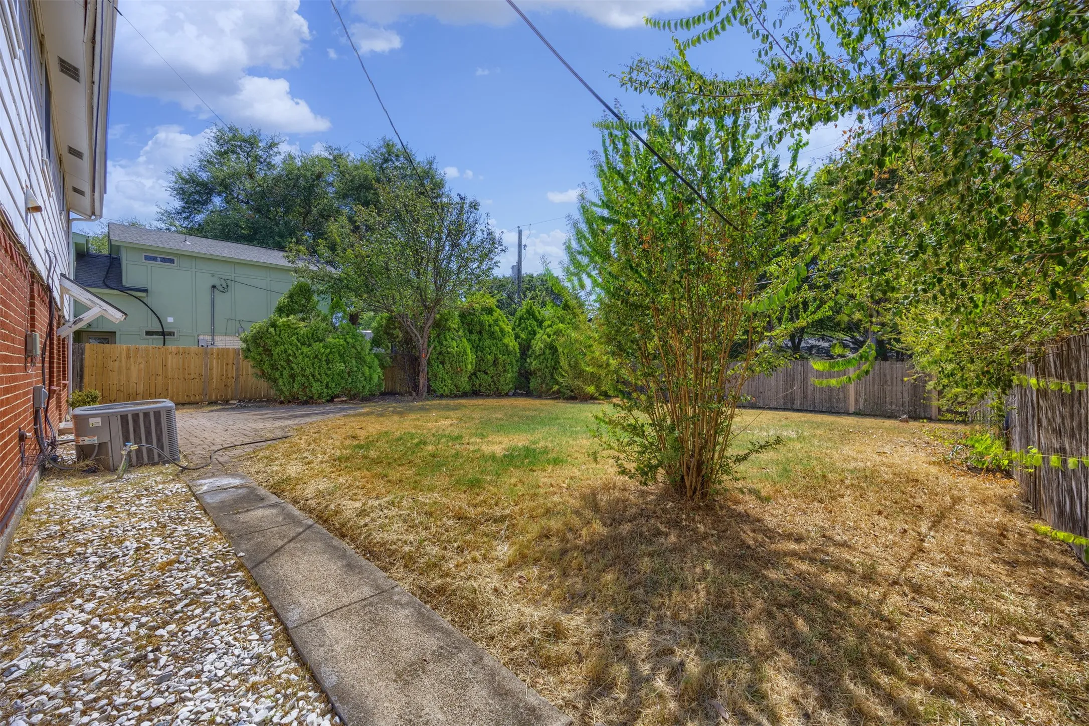 Expansive outdoor space featuring a concrete pathway, privacy fencing, and mature landscaping