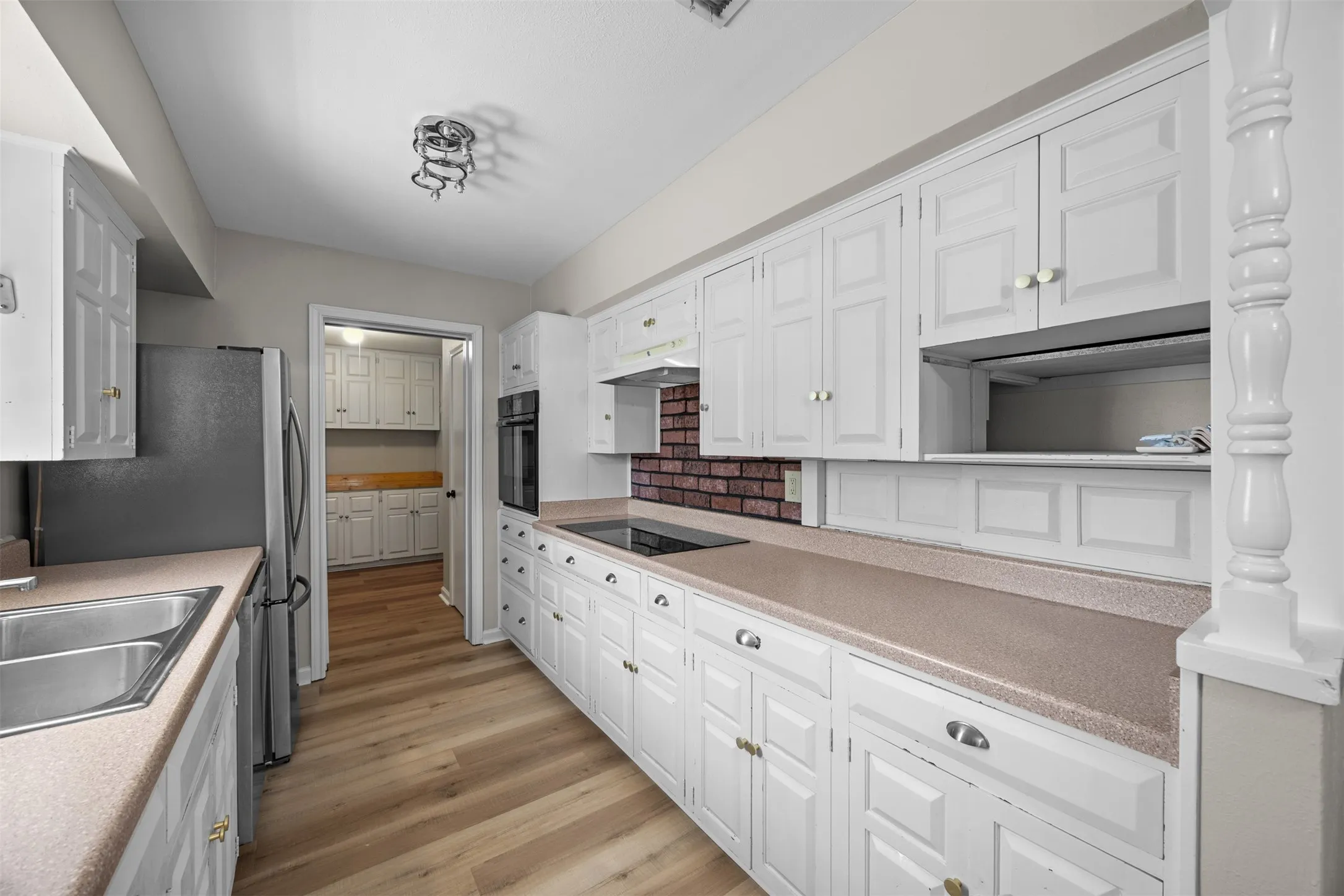 Galley kitchen with extensive white cabinetry, wood-finish flooring, built-in oven, integrated cooktop, and brick-patterned backsplash