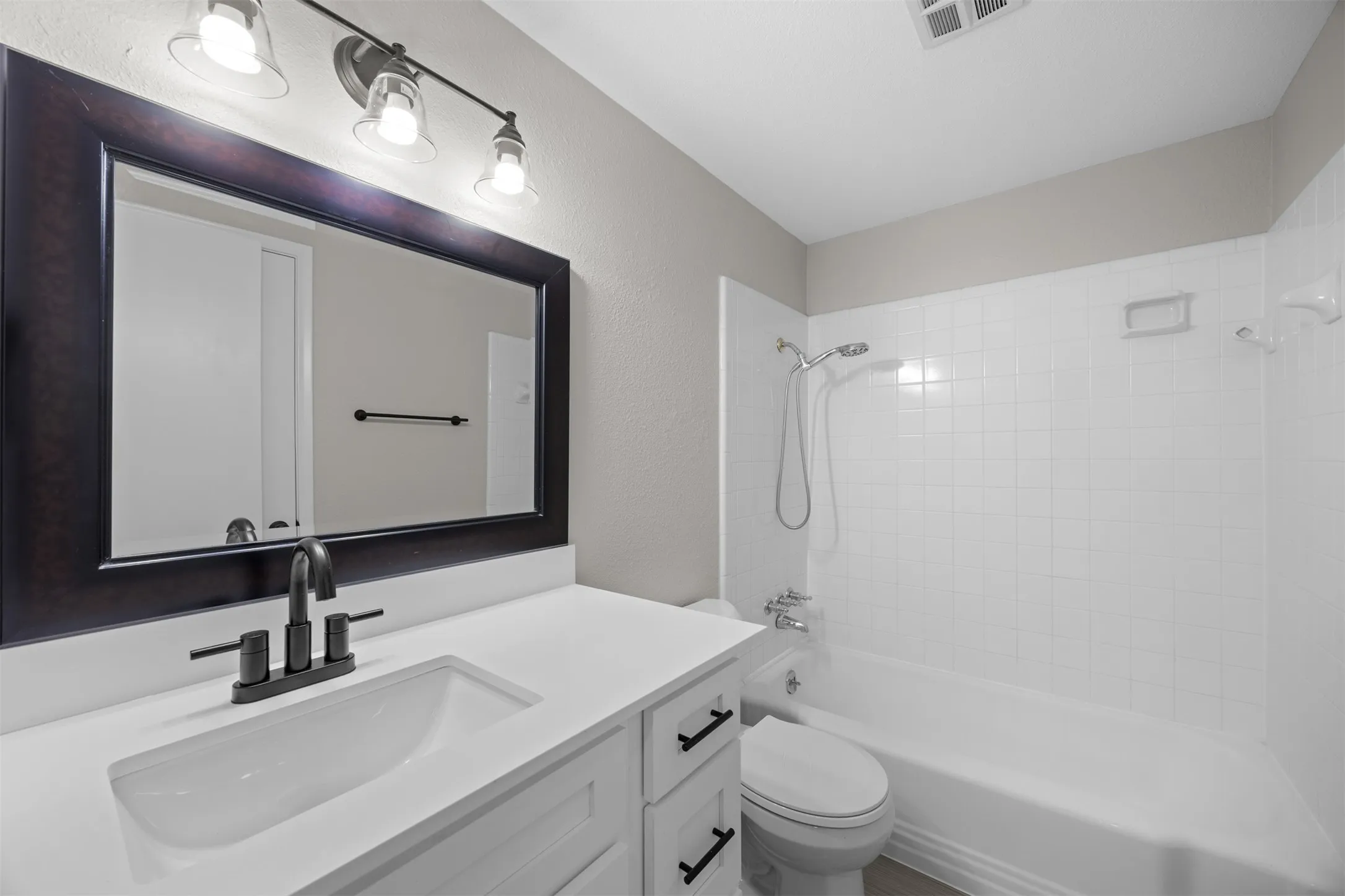 Bathroom featuring a white vanity with an integrated sink, dark wood-finish framed mirror, and a white tiled shower-tub combination