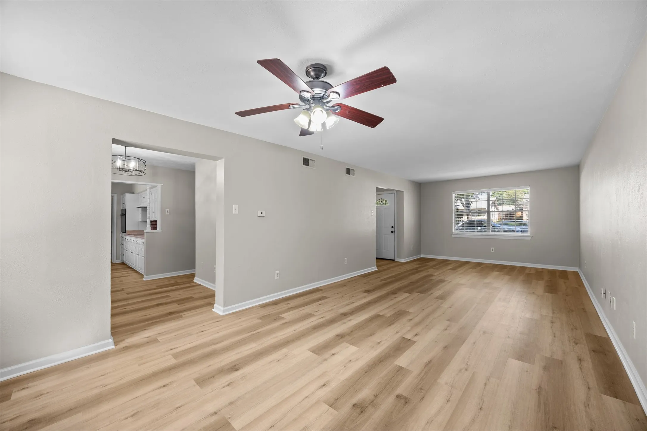 Spacious room featuring wood-finish flooring, a ceiling fan with integrated lighting, and neutral wall tones