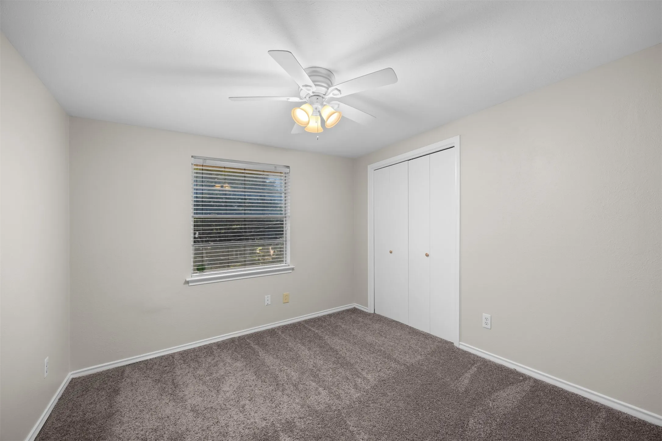 Recessed window with blinds, ceiling fan with light fixture, and double-door closet