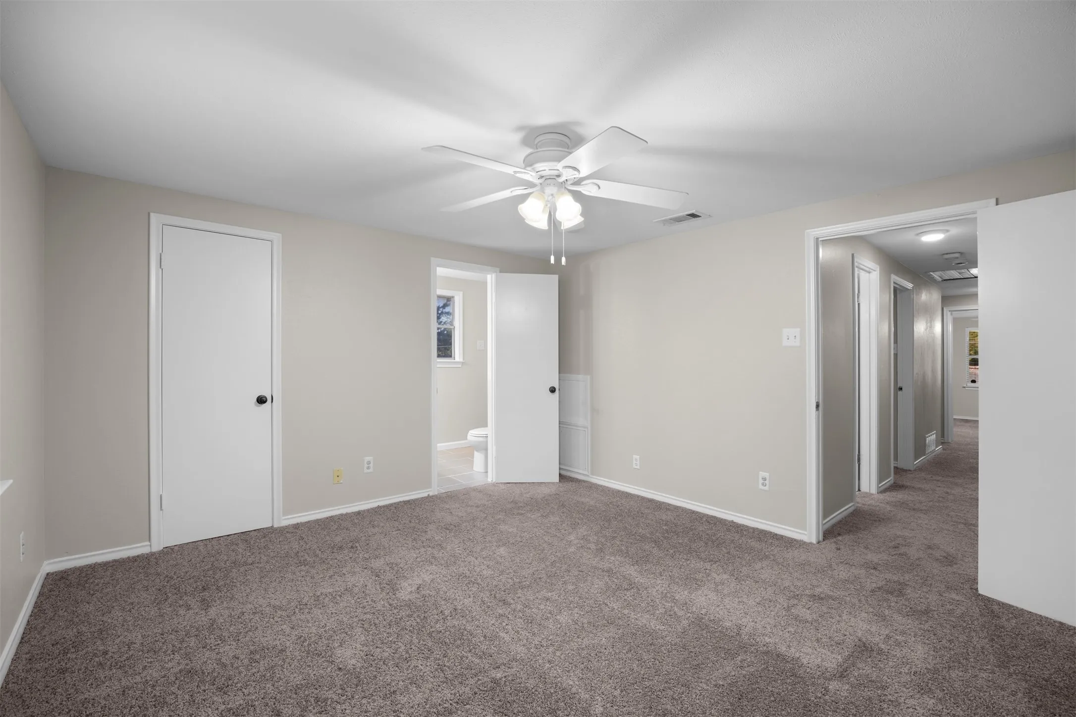 Neutral tone walls with white trim, brown carpet flooring, and a ceiling fan with integrated lighting
