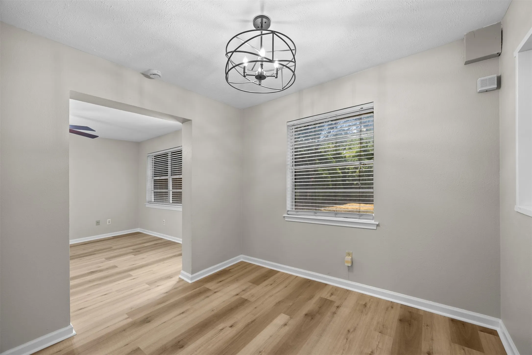 Open archway, wood-finish flooring, contemporary ceiling fixture, window with blinds, light wall color