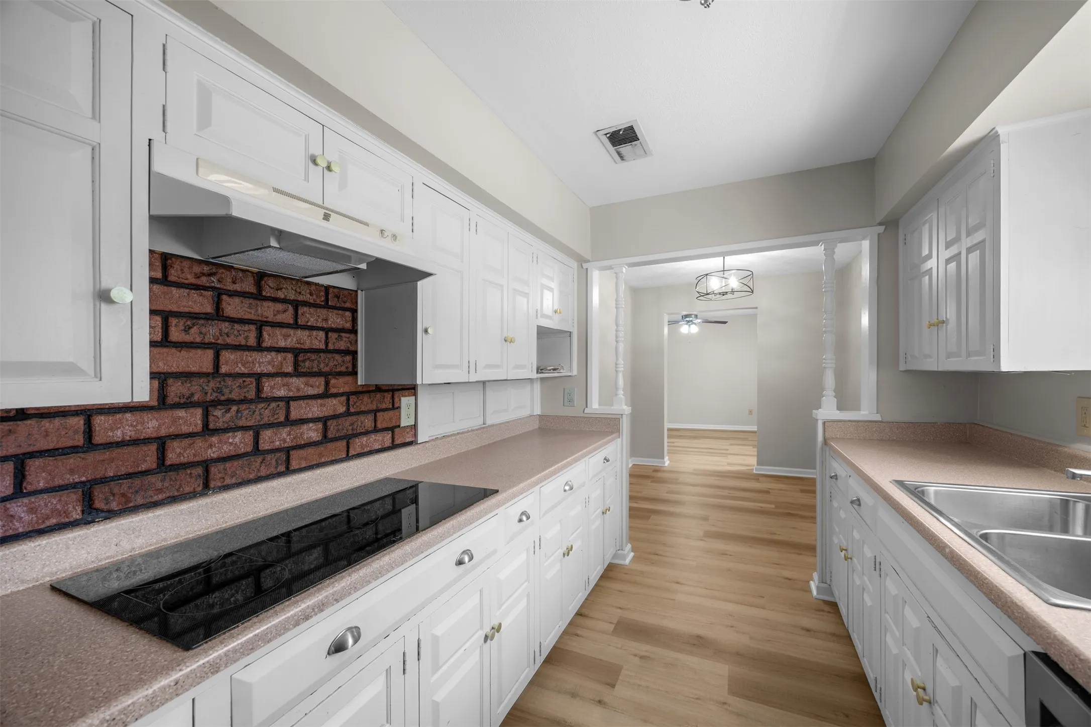 White cabinetry, brick backsplash, wood-finish flooring, built-in cooktop, and a double basin stainless steel sink