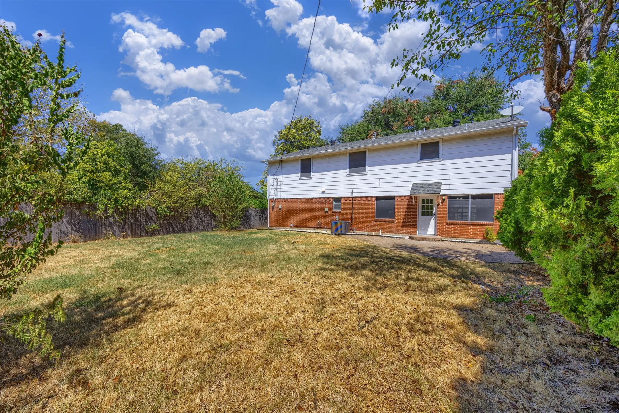 Expansive yard with natural landscaping, featuring a brick and white siding exterior