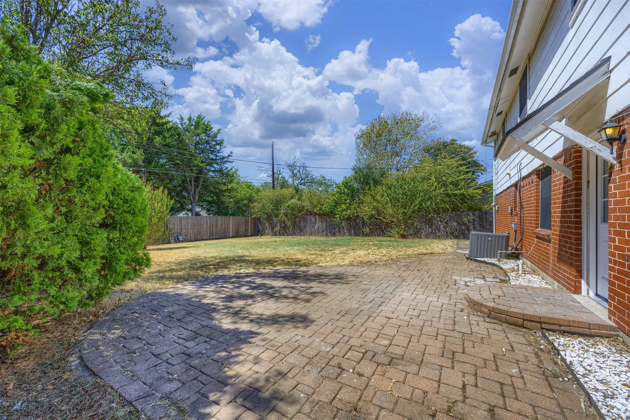Expansive backyard featuring a brick paver patio, full privacy fencing, mature landscaping, and a red brick exterior